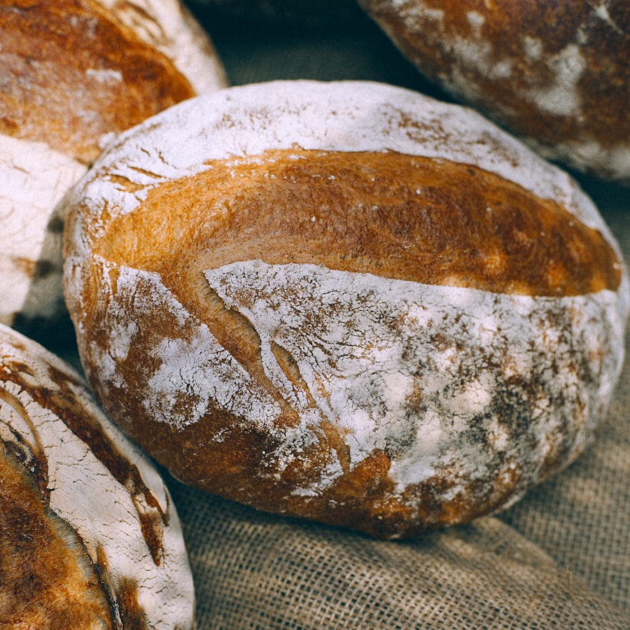 A round sourdough boule with a deeply scored, flour-dusted crust, cooling on burlap beside other loaves.